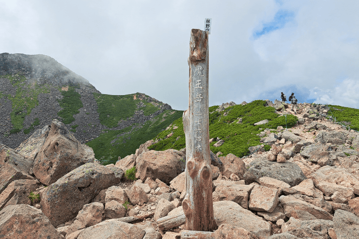 魔王岳山頂の標識とハイマツ帯の稜線を歩く登山者